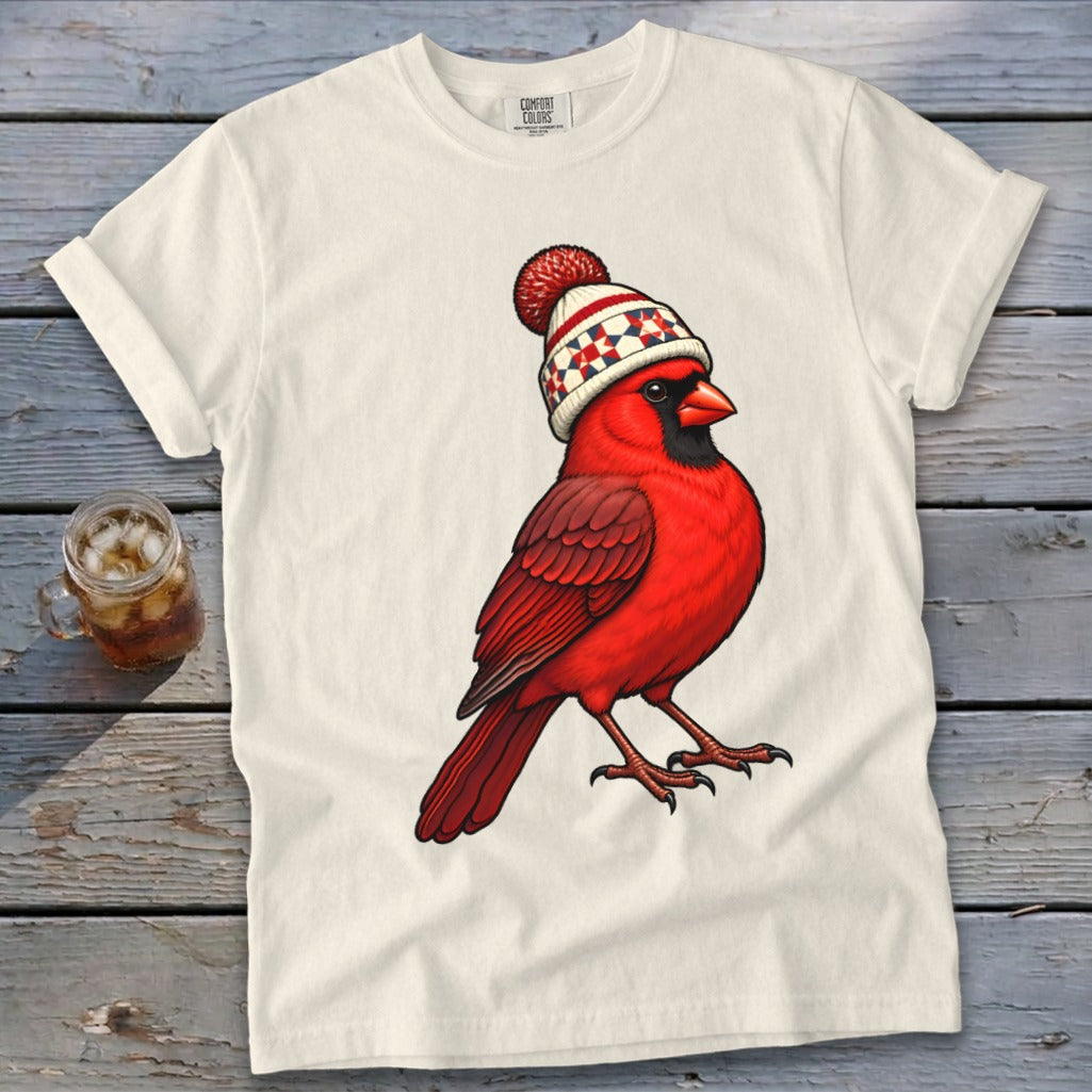 A white t-shirt featuring an illustration of a red cardinal wearing a winter beanie with a pom-pom.