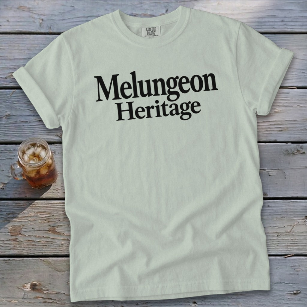 Light green crewneck t-shirt with rolled sleeves featuring the black text Melungeon Heritage on a wooden background.
