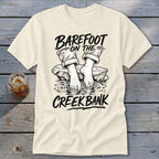 Cream t-shirt with "Barefoot on the Creek Bank" graphic of bare feet in water.