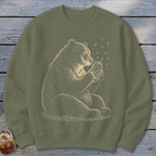 Bear holding a jar of stars with fireflies around, on a green sweatshirt.