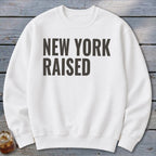 White sweatshirt with bold black text "NEW YORK RAISED" across the chest.