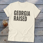 Cream t-shirt with "GEORGIA RAISED" in dark grey block letters.