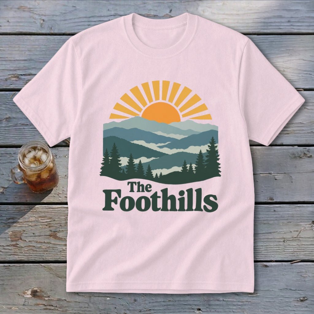 Pink t-shirt with mountains, sun, and "The Foothills" text graphic.
