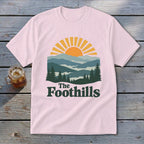 Pink t-shirt with mountains, sun, and "The Foothills" text graphic.
