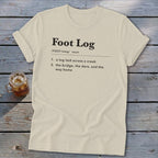 Beige t-shirt featuring dictionary-style text defining Foot Log laid across a wooden background next to a drink.