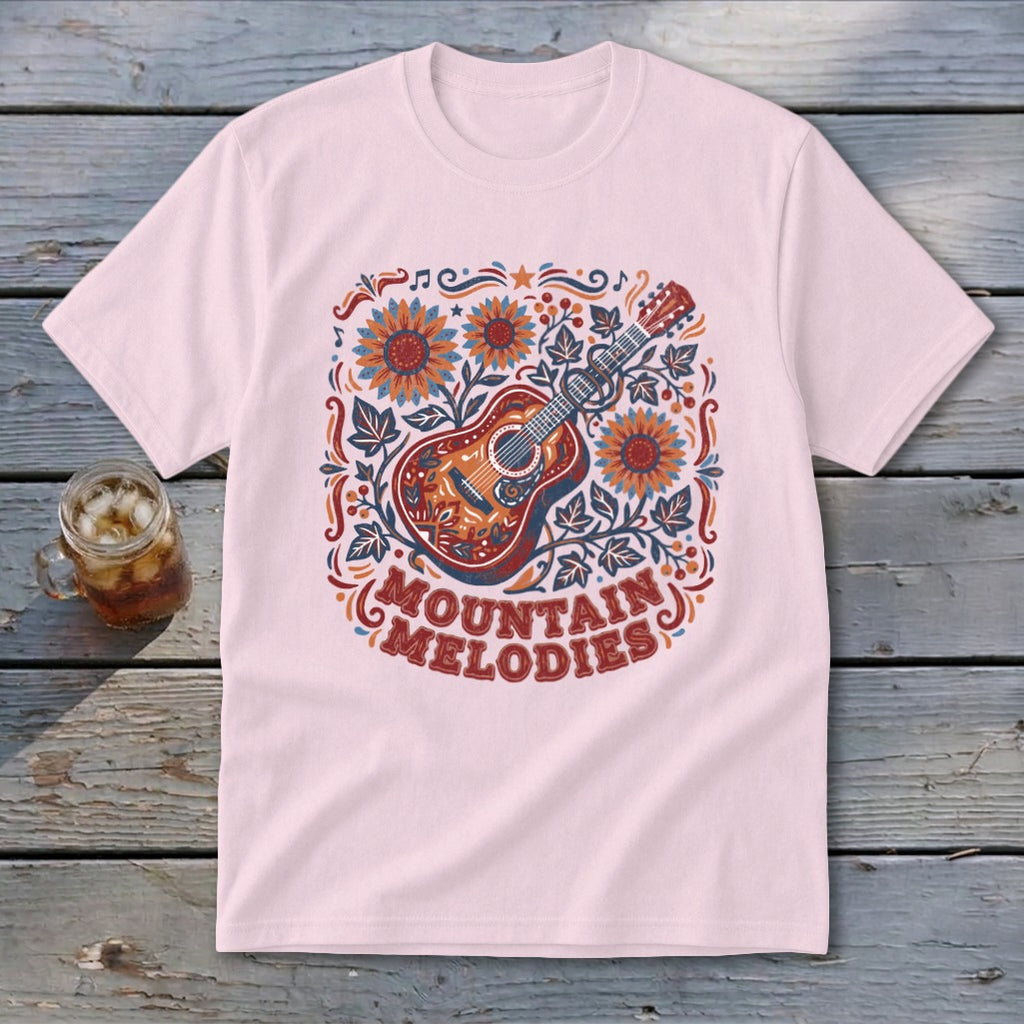 A light pink t-shirt with a vintage-style graphic of an acoustic guitar, sunflowers, and the text MOUNTAIN MELODIES.