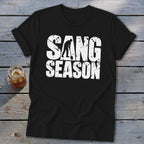 A black t-shirt with rolled sleeves features white distressed text reading SANG SEASON, with a silhouetted digger forming the letter A.