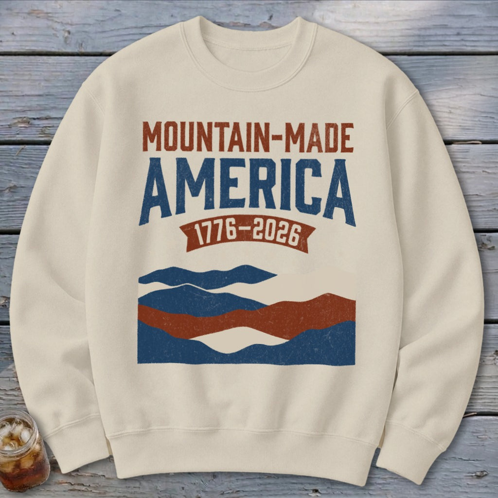 Beige crewneck sweatshirt featuring a retro Mountain-Made America graphic with mountains and the text 1776-2026.