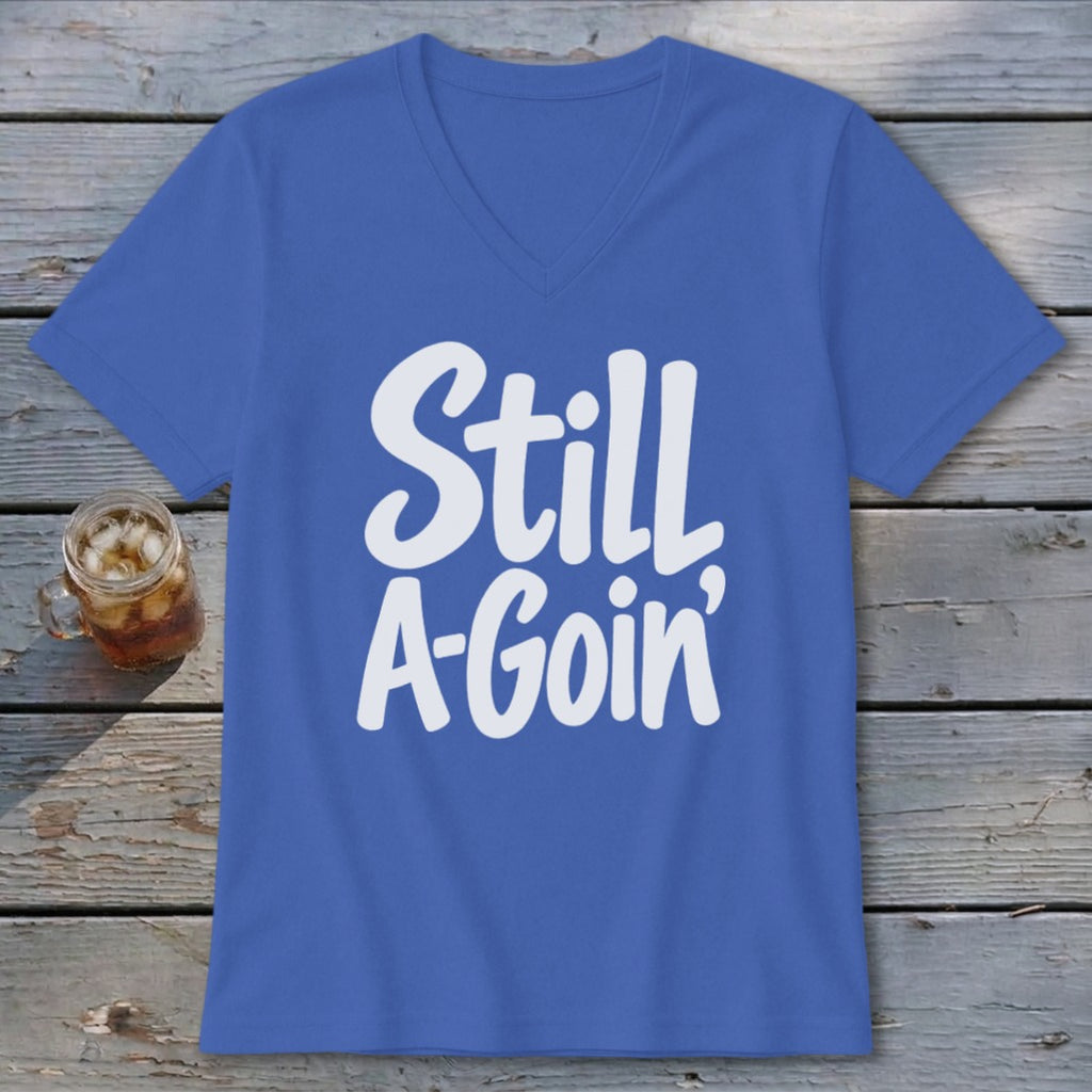 Blue V-neck t-shirt with white text reading Still A-Goin' on a wooden surface.