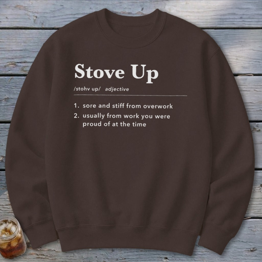 A brown crewneck sweatshirt featuring white text defining the term Stove Up on a rustic wooden background.