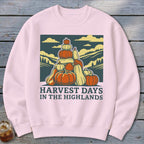 A light pink crewneck sweatshirt featuring a graphic of stacked pumpkins and mountains with text reading HARVEST DAYS IN THE HIGHLANDS.
