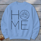 Light blue crewneck sweatshirt featuring a black minimalist design with the word HOME, where the O is replaced by a mountain and sun graphic.