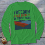 A green long-sleeve t-shirt features text and a graphic of layered hills on a wooden surface.