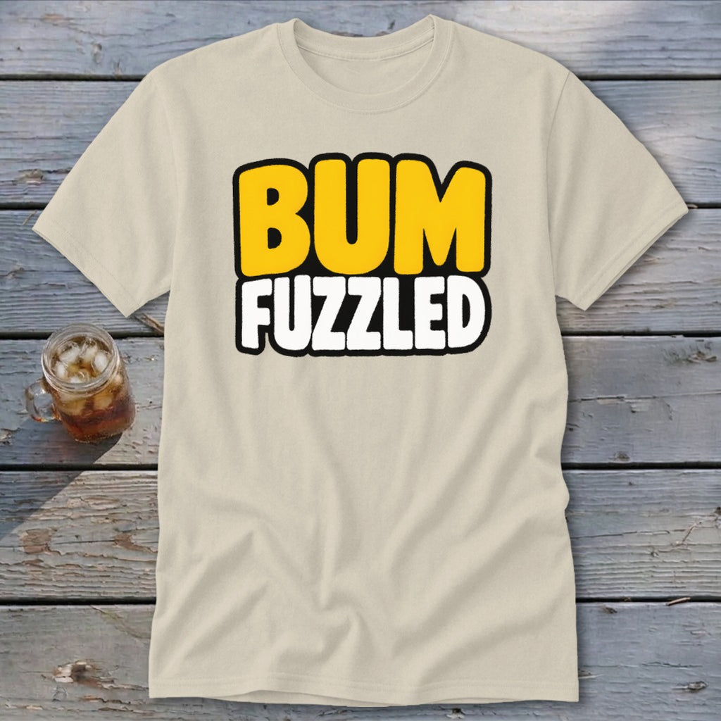 A cream-colored t-shirt rests on a wooden surface, featuring the black-bordered text BUM FUZZLED in yellow and white.