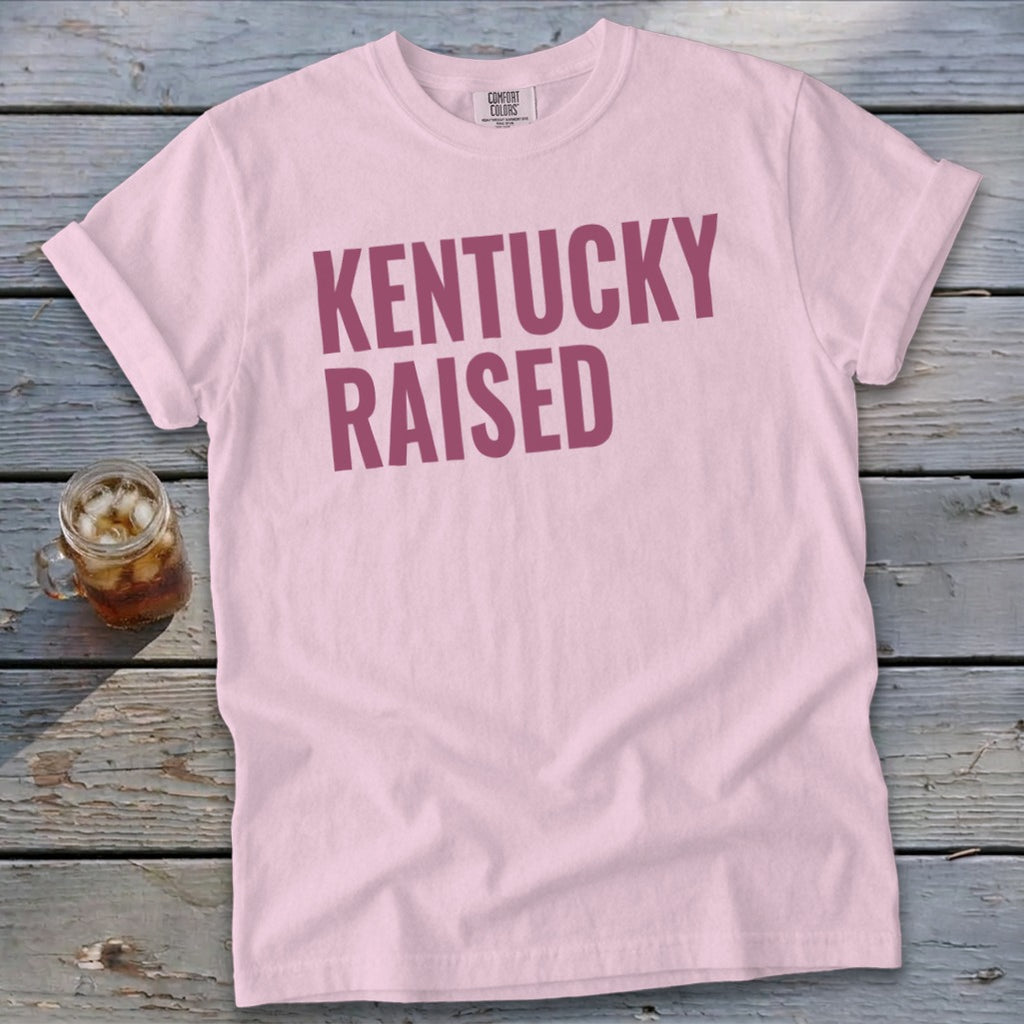 Pink t-shirt with maroon "Kentucky Raised" text and a drink.