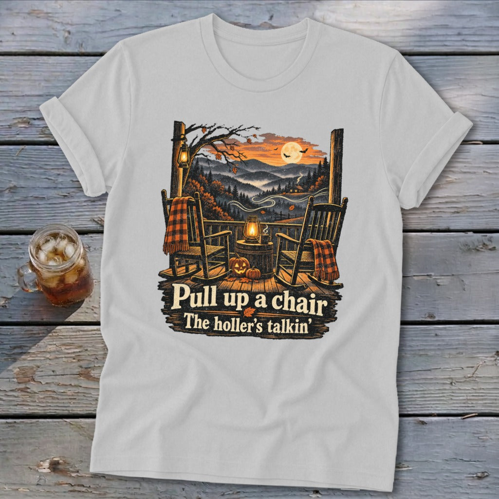 T-shirt graphic with rocking chairs on a porch overlooking mountains at sunset, text reads "Pull up a chair The holler's talkin'".