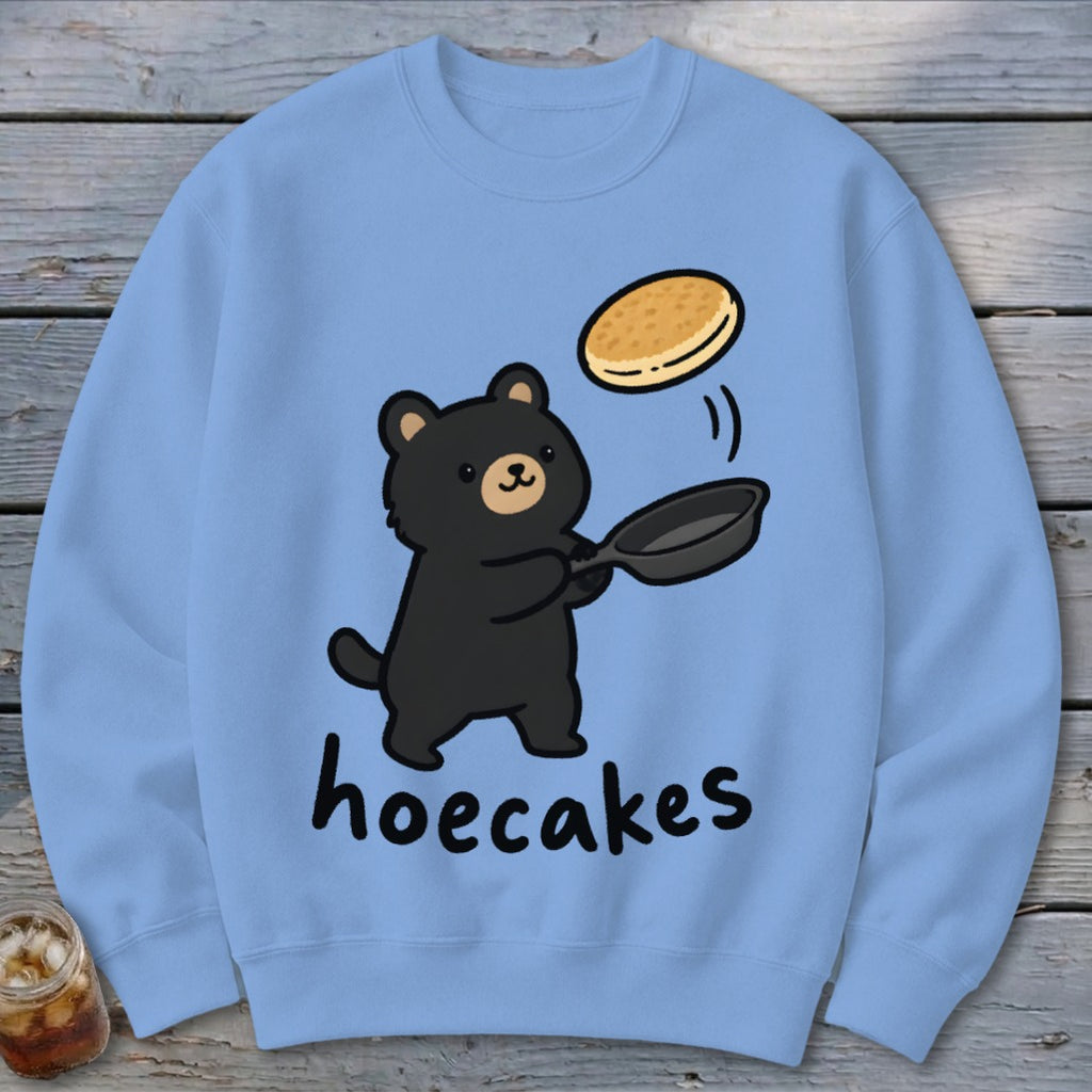 Light blue crewneck sweatshirt featuring a cartoon black bear flipping a pancake and the text hoecakes.