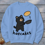 Light blue crewneck sweatshirt featuring a cartoon black bear flipping a pancake and the text hoecakes.