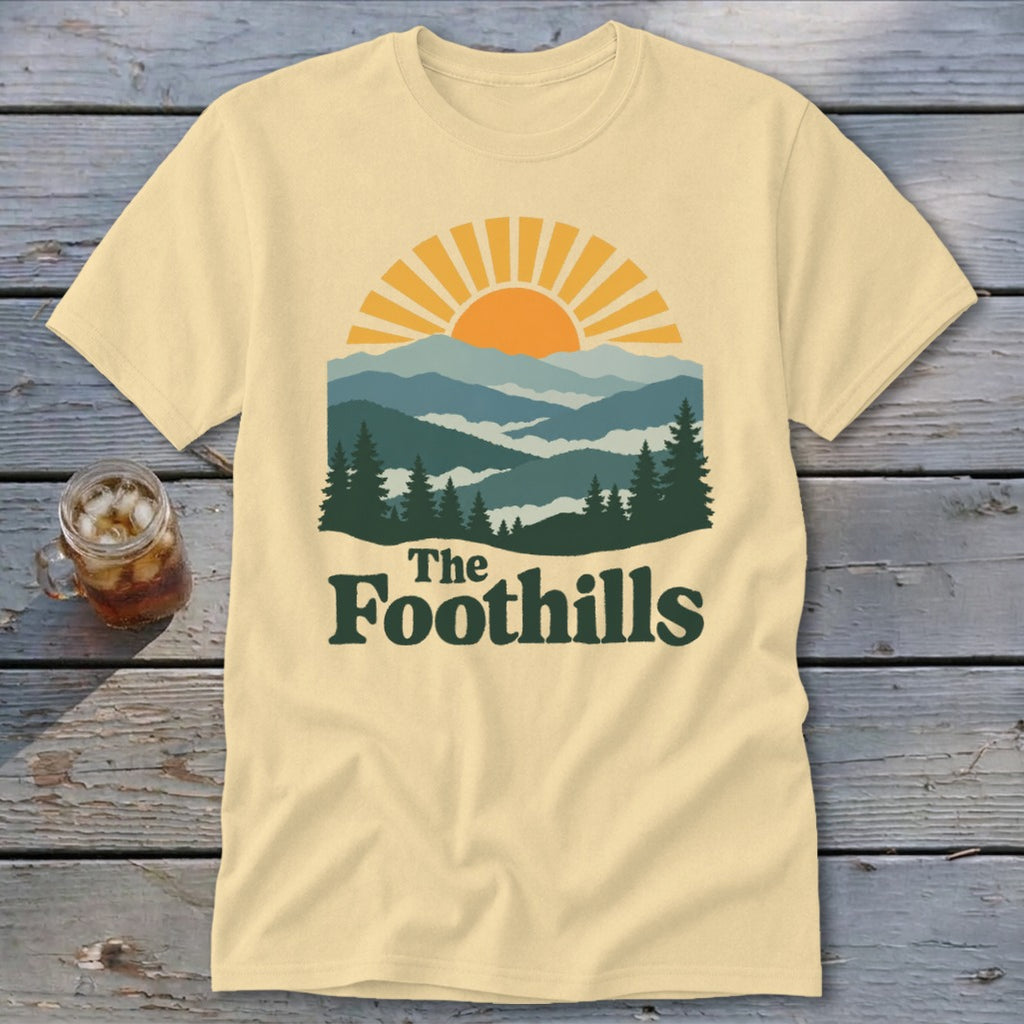Cream t-shirt with sun, mountains, trees, and "The Foothills" text.