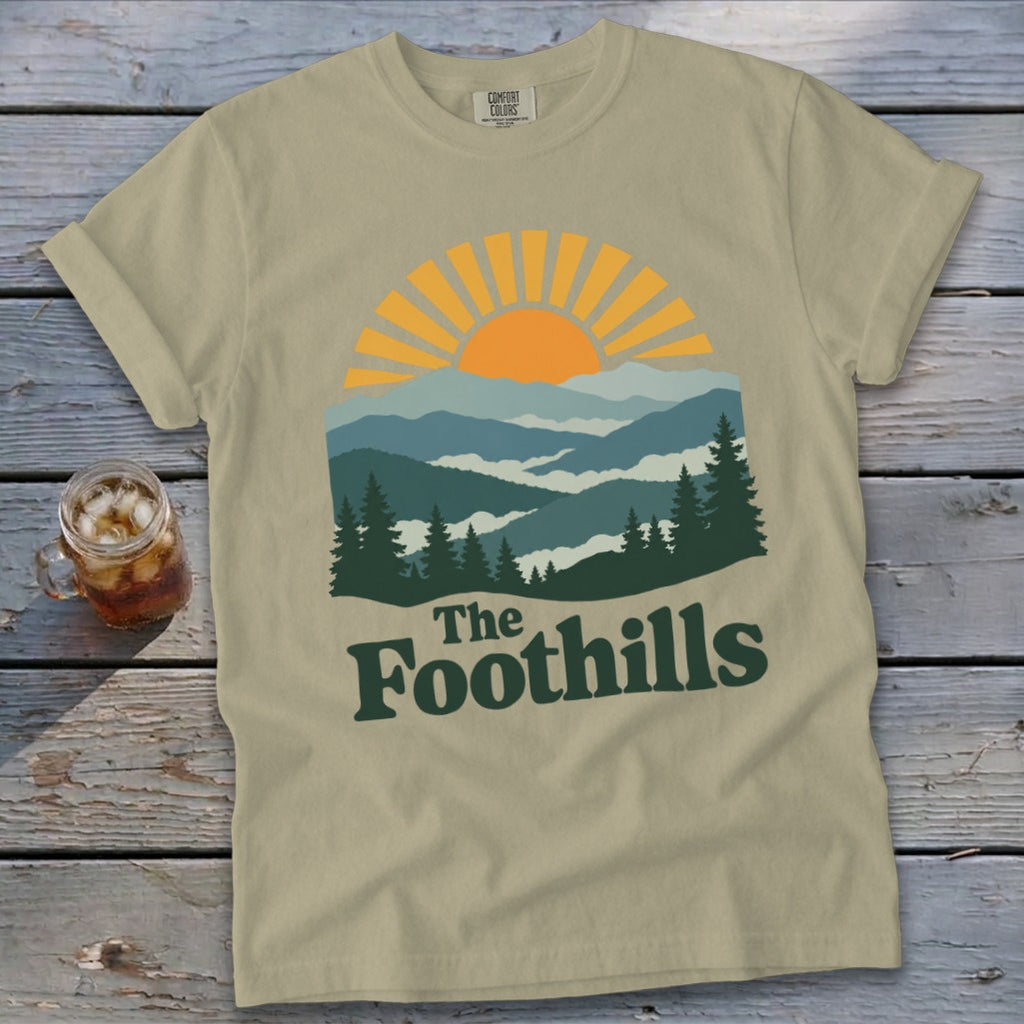 Khaki t-shirt with "The Foothills" graphic featuring mountains and a sunrise.