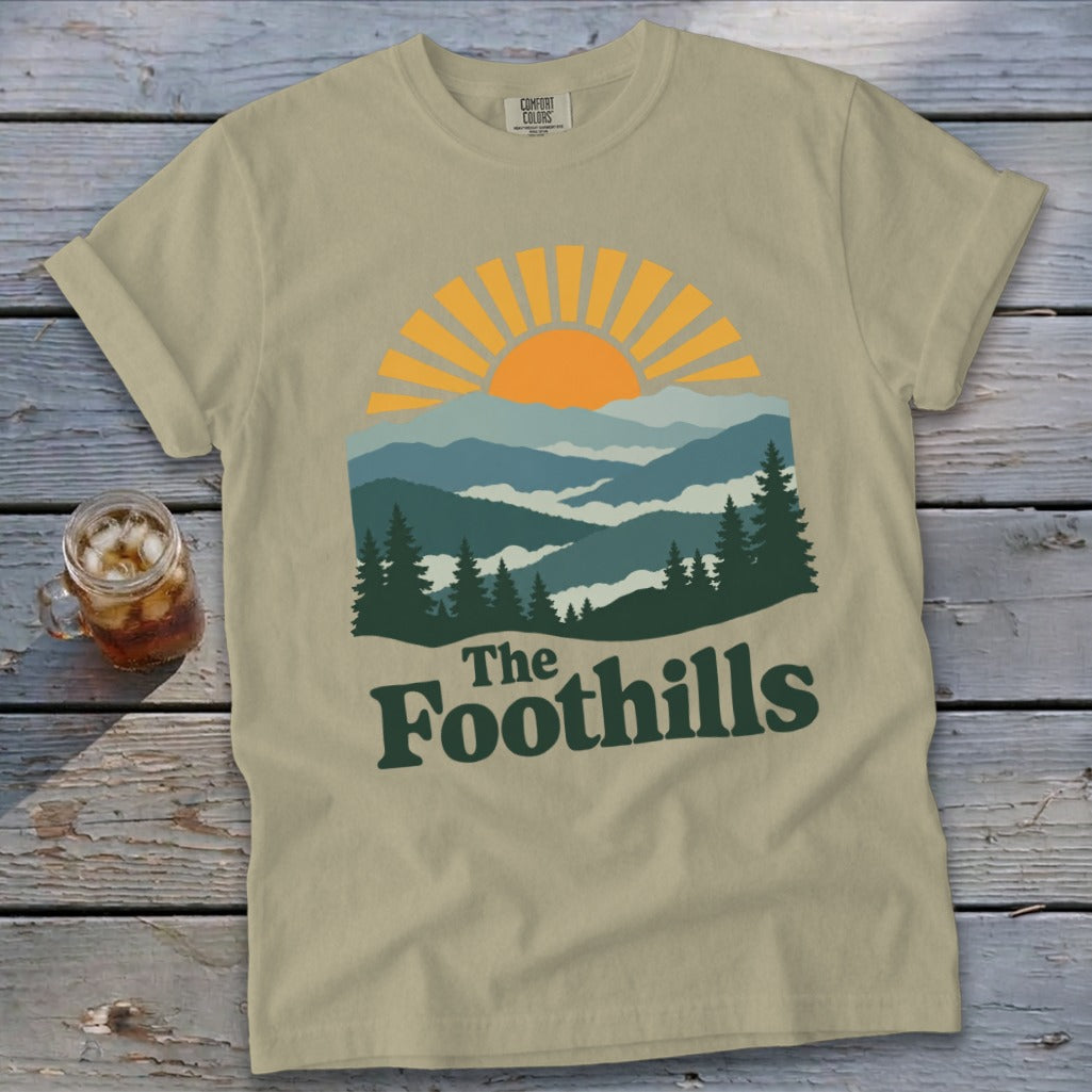 Khaki t-shirt with "The Foothills" graphic featuring mountains and a sunrise.