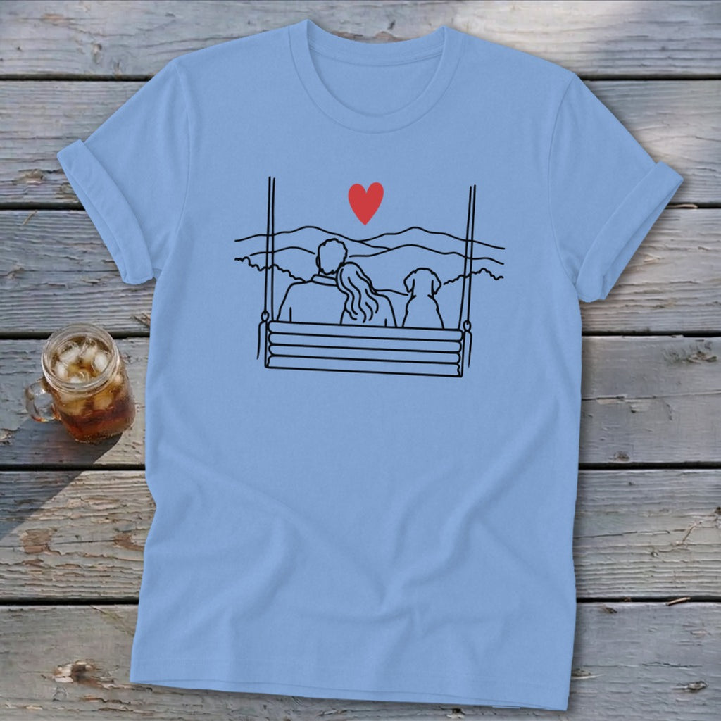 Light blue t-shirt with line art of couple and dog on swing, red heart, mountains.
