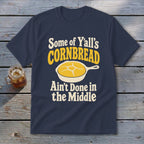 Navy blue t-shirt featuring the text "Some of Y'all's Cornbread Ain't Done in the Middle" above and below a skillet of cornbread.