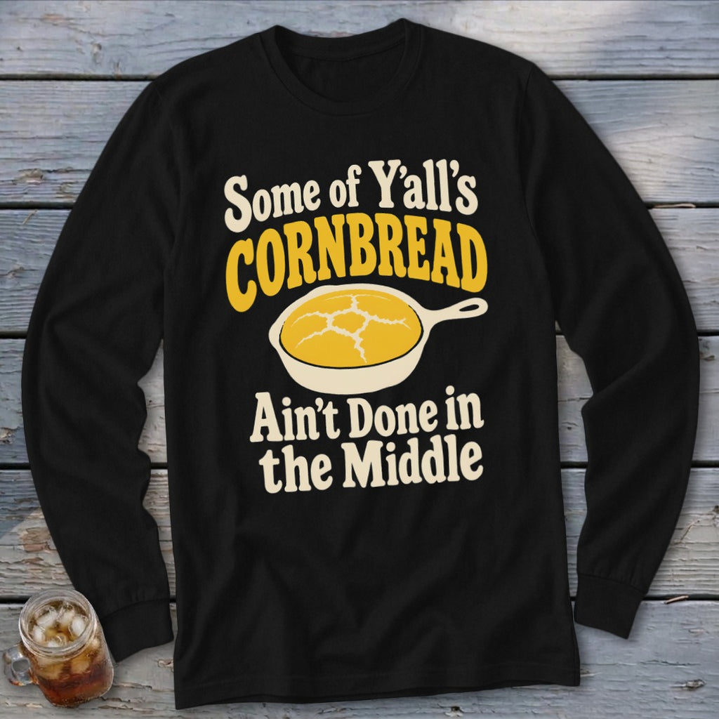 Black long-sleeve t-shirt with text reading Some of Y'all's Cornbread Ain't Done in the Middle above a graphic of cornbread in a skillet.