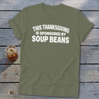 An olive green crewneck t-shirt with white text reading THIS THANKSGIVING IS SPONSORED BY SOUP BEANS.