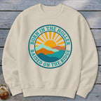 A cream crewneck sweatshirt featuring a circular graphic with mountains, a rising sun, and text that reads BORN IN THE HOLLER RAISED ON THE RIDGE.