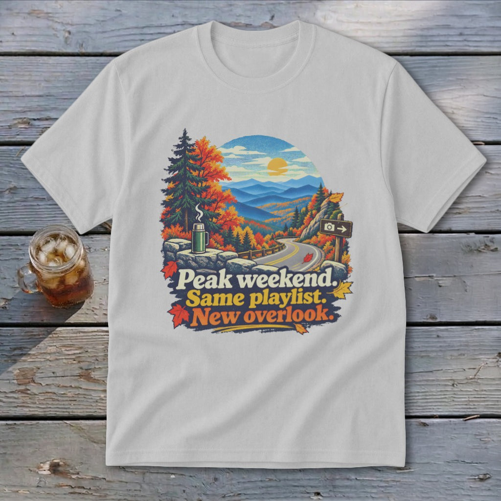 White t-shirt with colorful graphic of mountains, autumn trees, and text "Peak weekend. Same playlist. New overlook."
