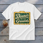 A white t-shirt featuring a green vintage marquee sign graphic that reads Dinner on the Grounds.