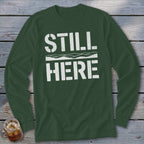 Dark green long sleeve t-shirt with white text "STILL HERE" and wavy lines.