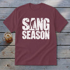 Maroon t-shirt featuring white distressed text reading "SANG SEASON" with a silhouette of a person digging.