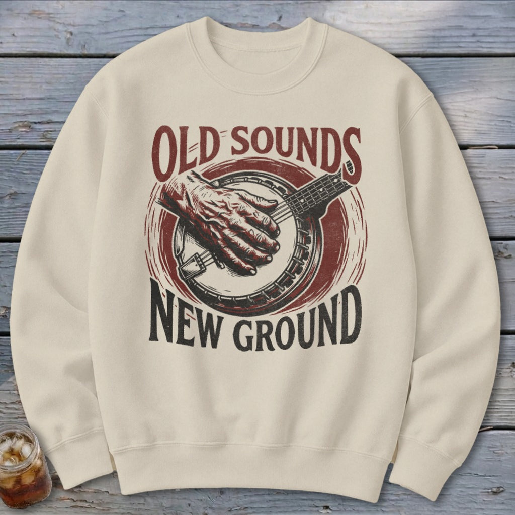 Beige crewneck sweatshirt featuring a vintage graphic of a hand playing a banjo with the text "OLD SOUNDS NEW GROUND".