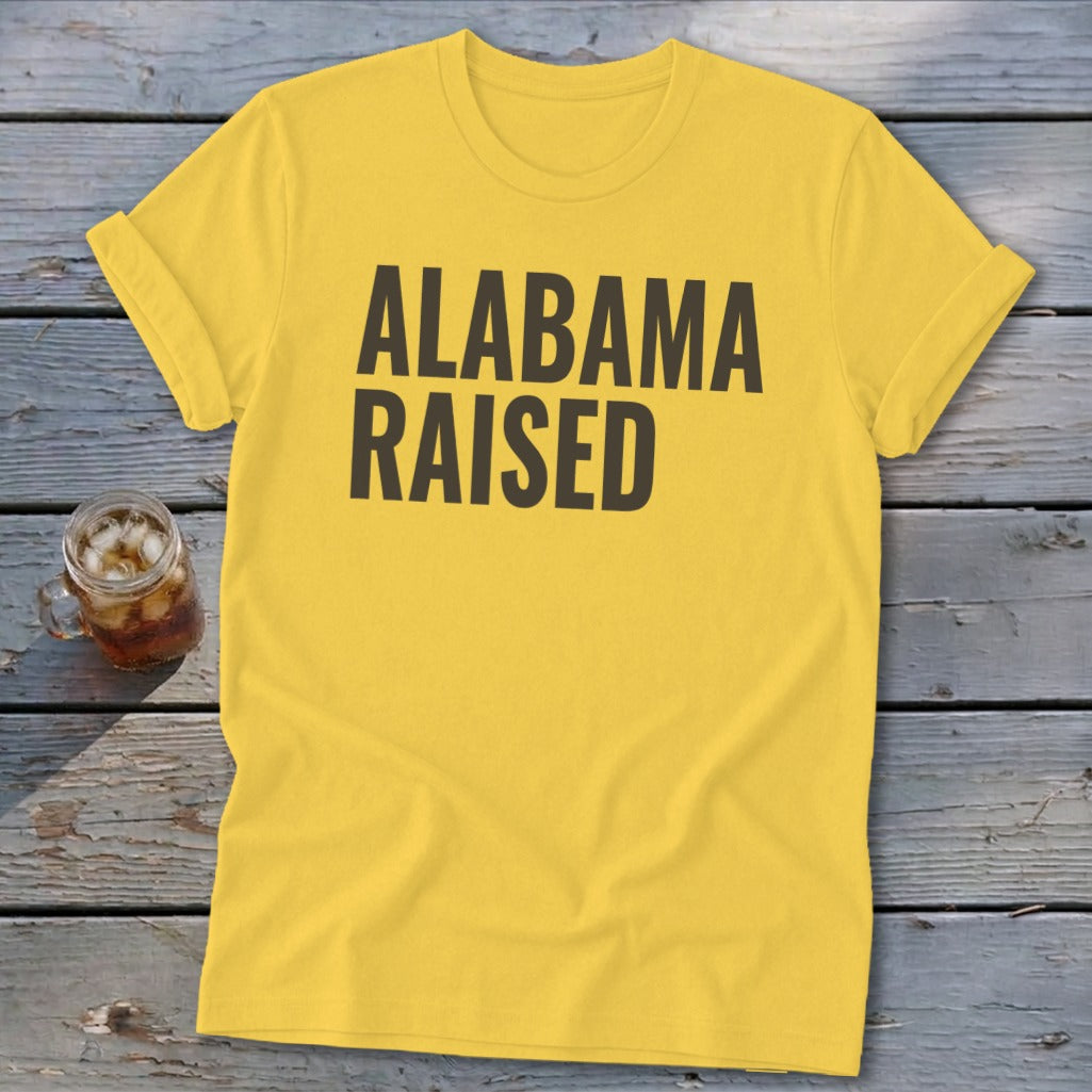 Yellow t-shirt with bold black text reading "ALABAMA RAISED".