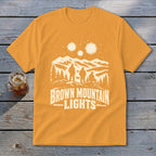 Gold t-shirt featuring a white graphic of three figures, mountains, and the text Brown Mountain Lights.