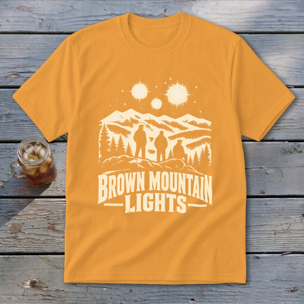 Gold t-shirt featuring a white graphic of three figures, mountains, and the text Brown Mountain Lights.