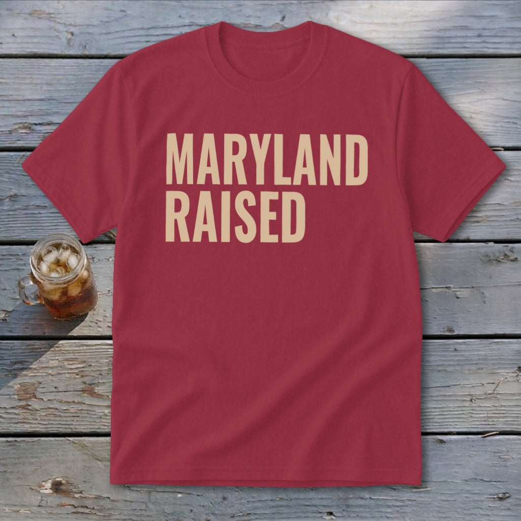 Crimson t-shirt with "MARYLAND RAISED" text in tan, next to a glass of iced beverage.