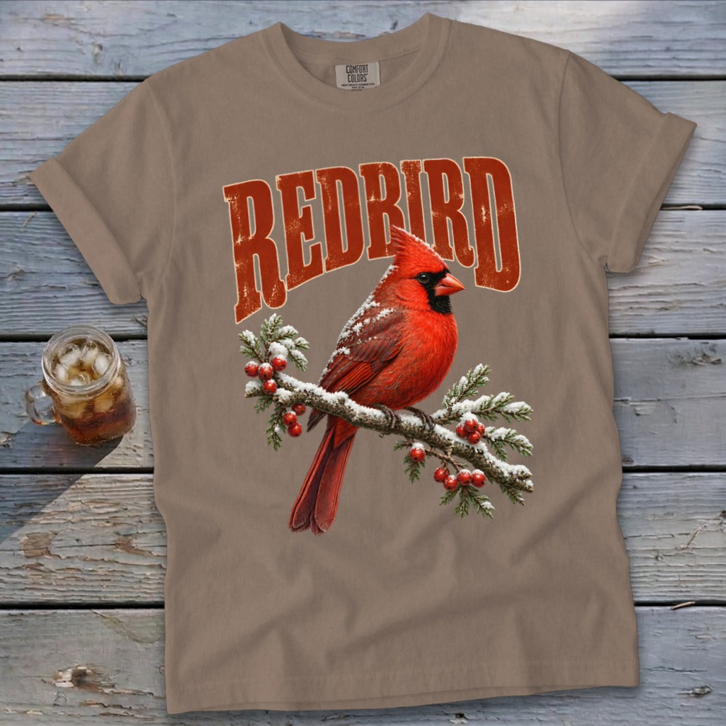 Taupe t-shirt featuring a red cardinal perched on a snowy pine branch with red berries and the text REDBIRD.