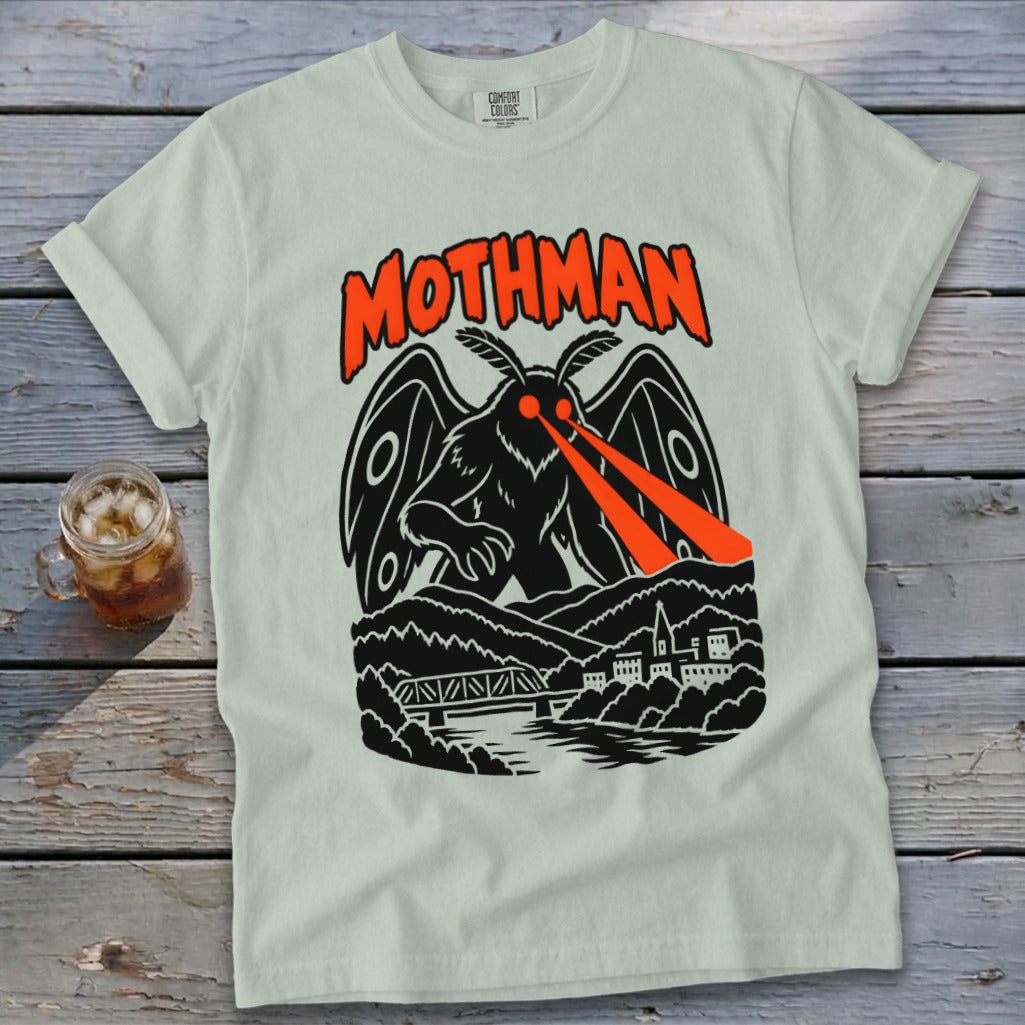 Light-colored t-shirt with black and orange Mothman graphic, featuring the creature over a town and bridge.