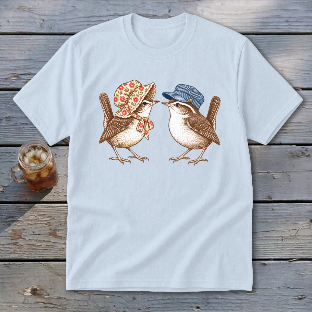 Two wrens, one in a floral bonnet and the other in a striped cap, face each other on a light blue t-shirt.