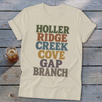Cream t-shirt featuring stacked retro text in green, brown, blue, yellow, and grey on wooden boards.