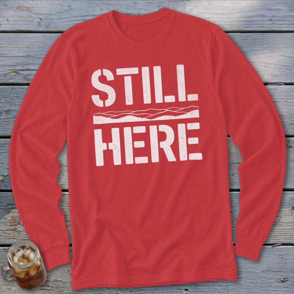 Red long sleeve shirt with white text that reads "STILL HERE".