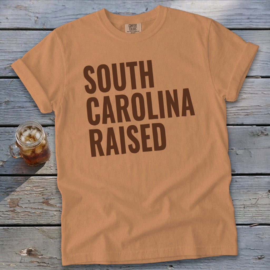 Orange t-shirt with "South Carolina Raised" text and a drink.