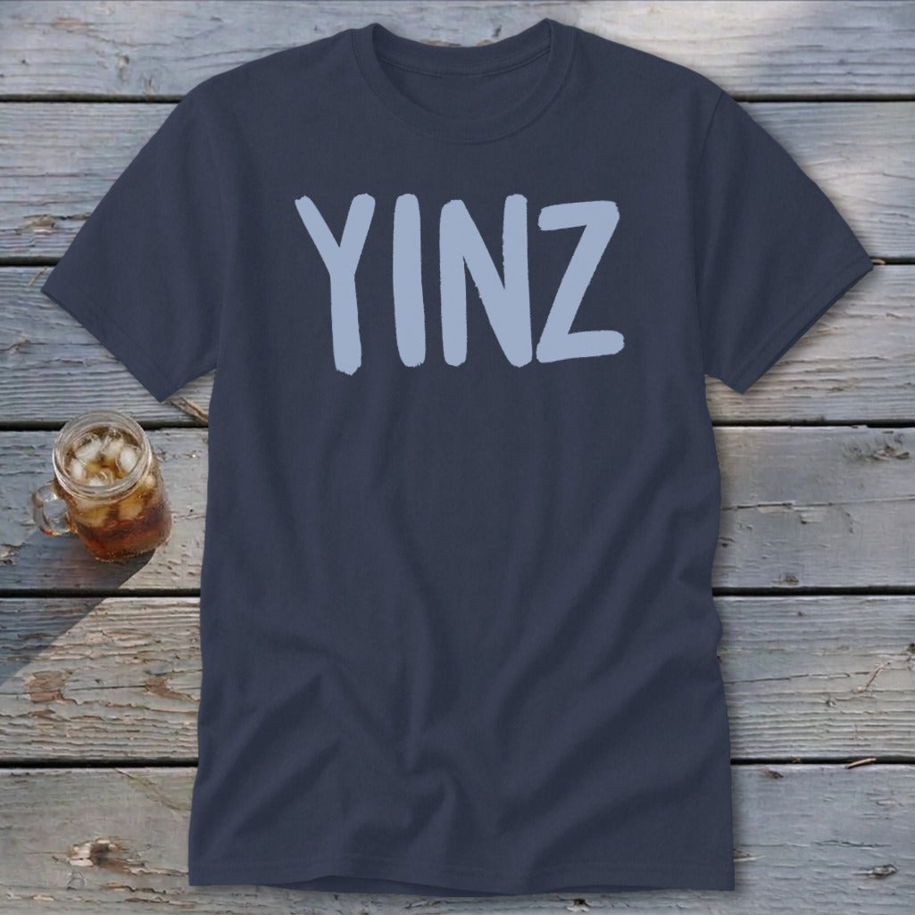 Navy t-shirt with light blue "YINZ" text, glass of iced drink beside it.