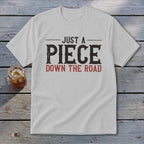 White t-shirt with black and red text "Just a Piece Down the Road".