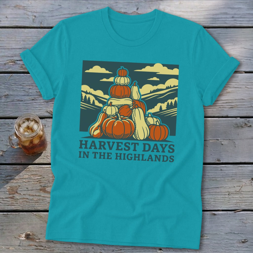 A turquoise t-shirt featuring a graphic of a large stack of pumpkins and the text "HARVEST DAYS IN THE HIGHLANDS".