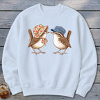 Two wrens wearing hats and scarves face each other on a light blue sweatshirt.