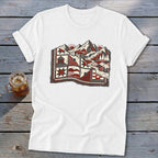 A white t-shirt features a red, black, and white graphic combining a landscape and quilt patterns.